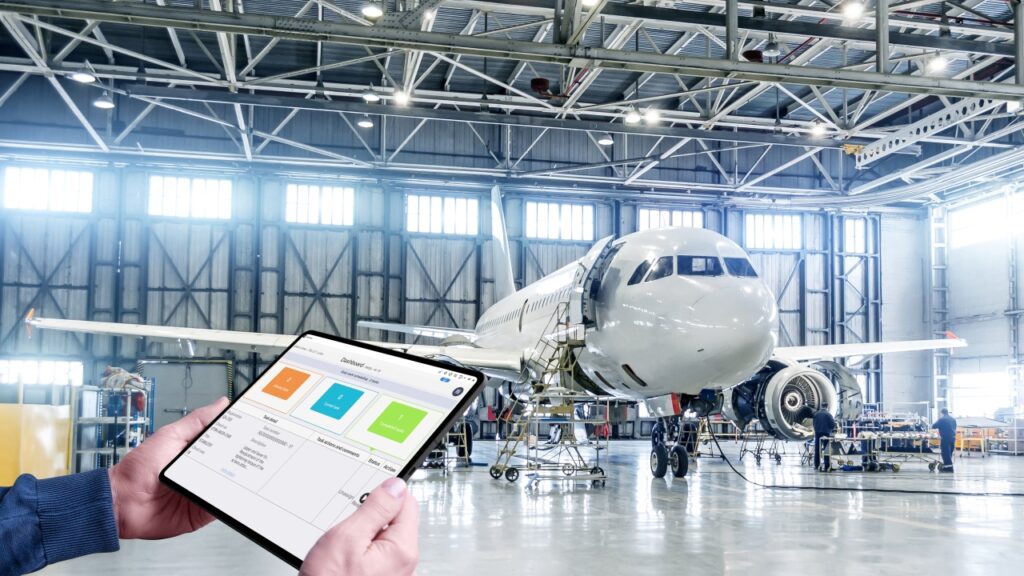 an iPad held in hands and in background there is an airplane is being repaired by engineers in a warehouse representing of Ameen projects